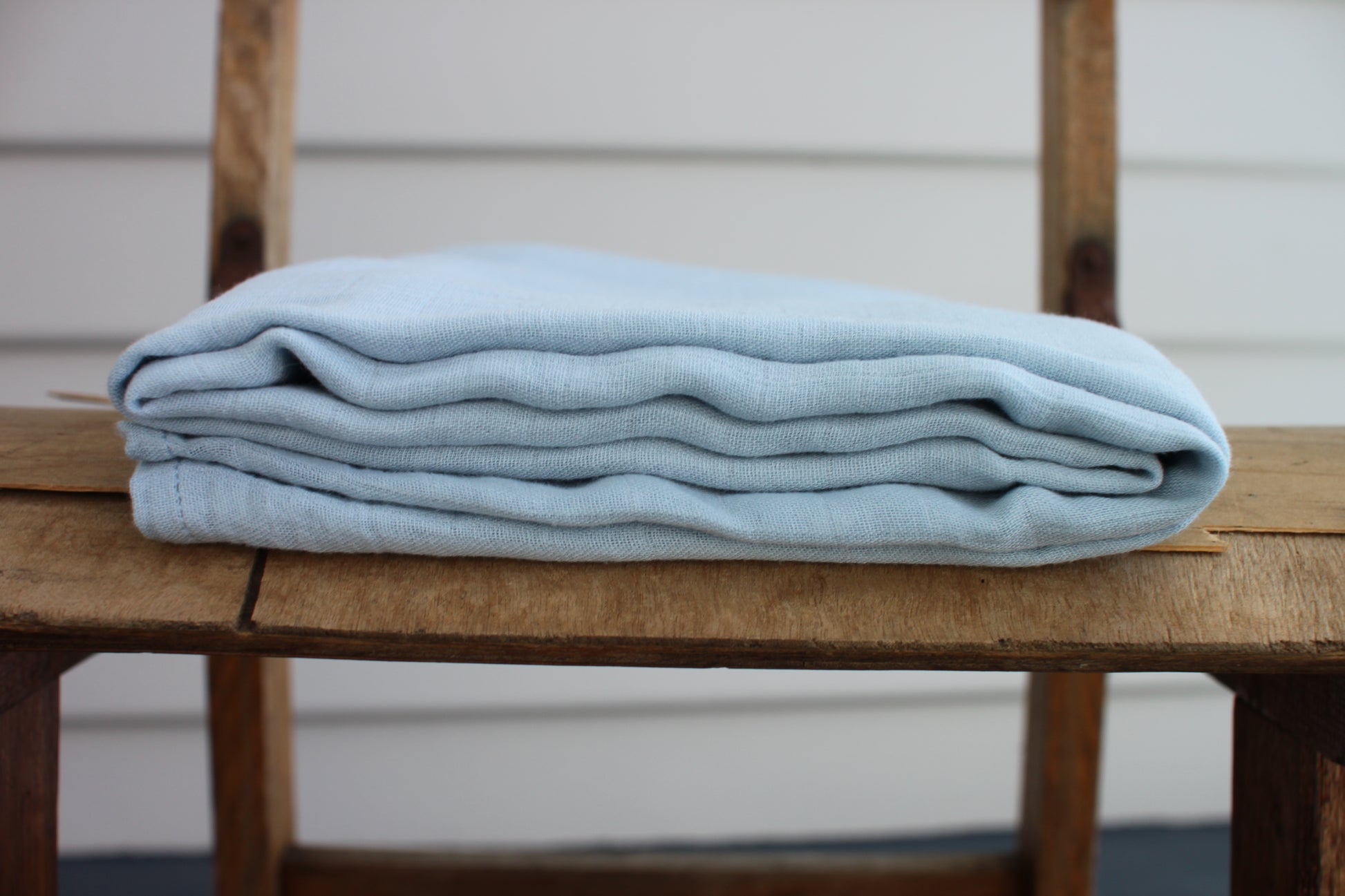 One sky blue muslin cloth sits folded on a wooden chair. 