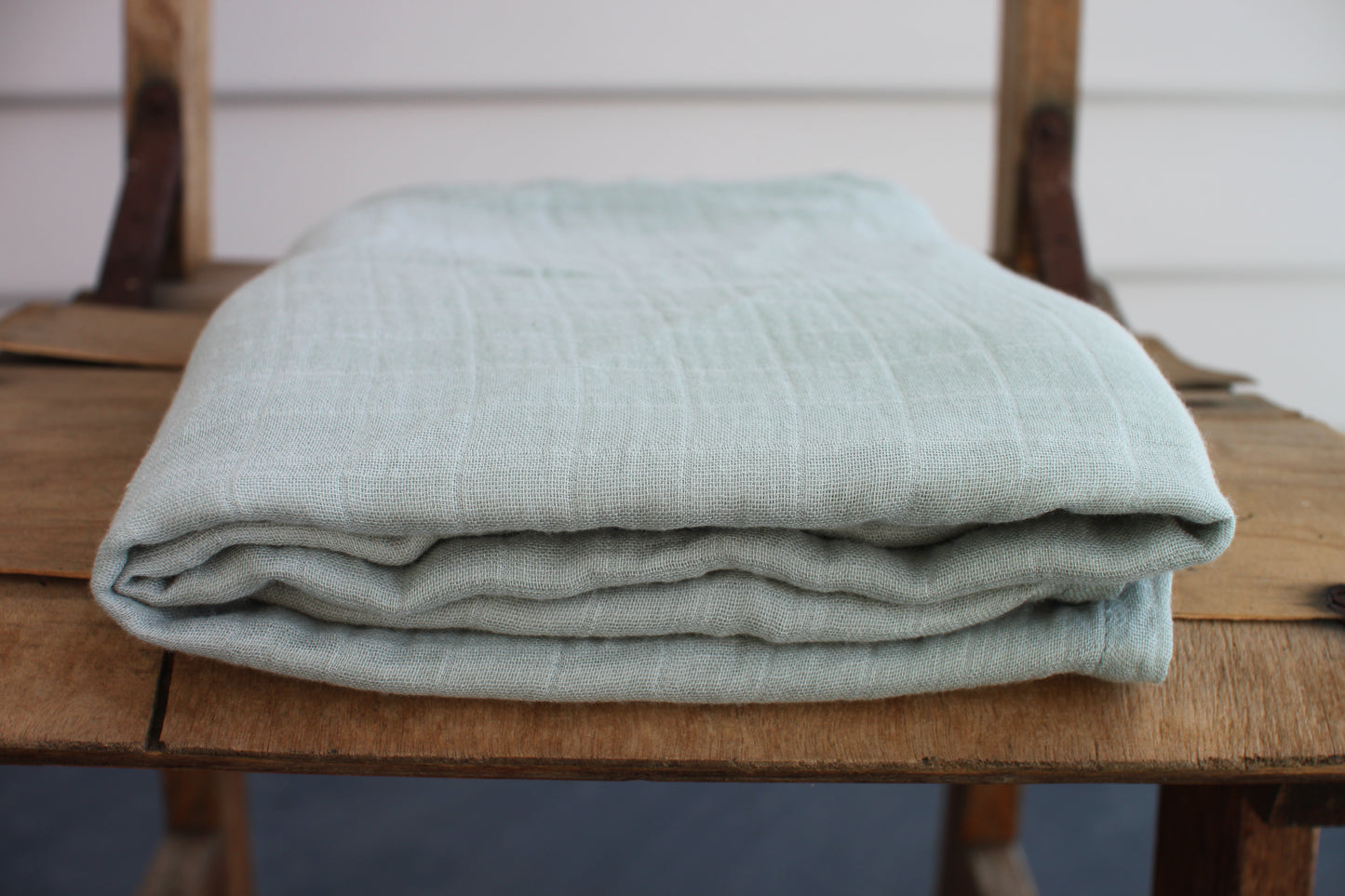 One moss green muslin cloth sits folded on a wooden chair. 