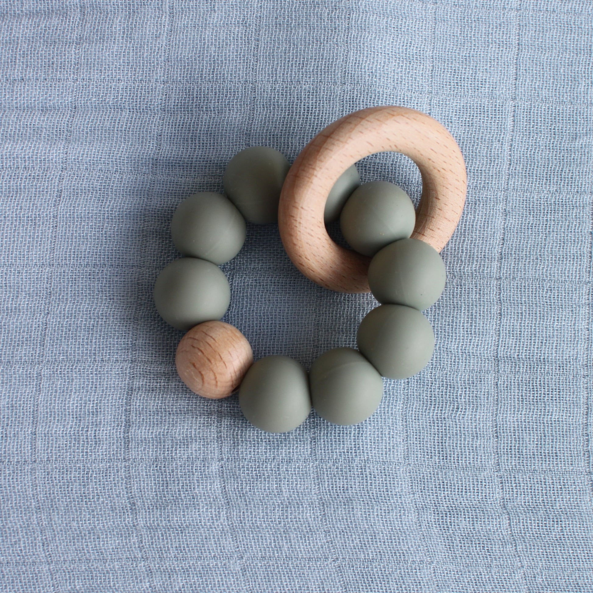 A silicone and beech wood teether. The silicone beads are green. 