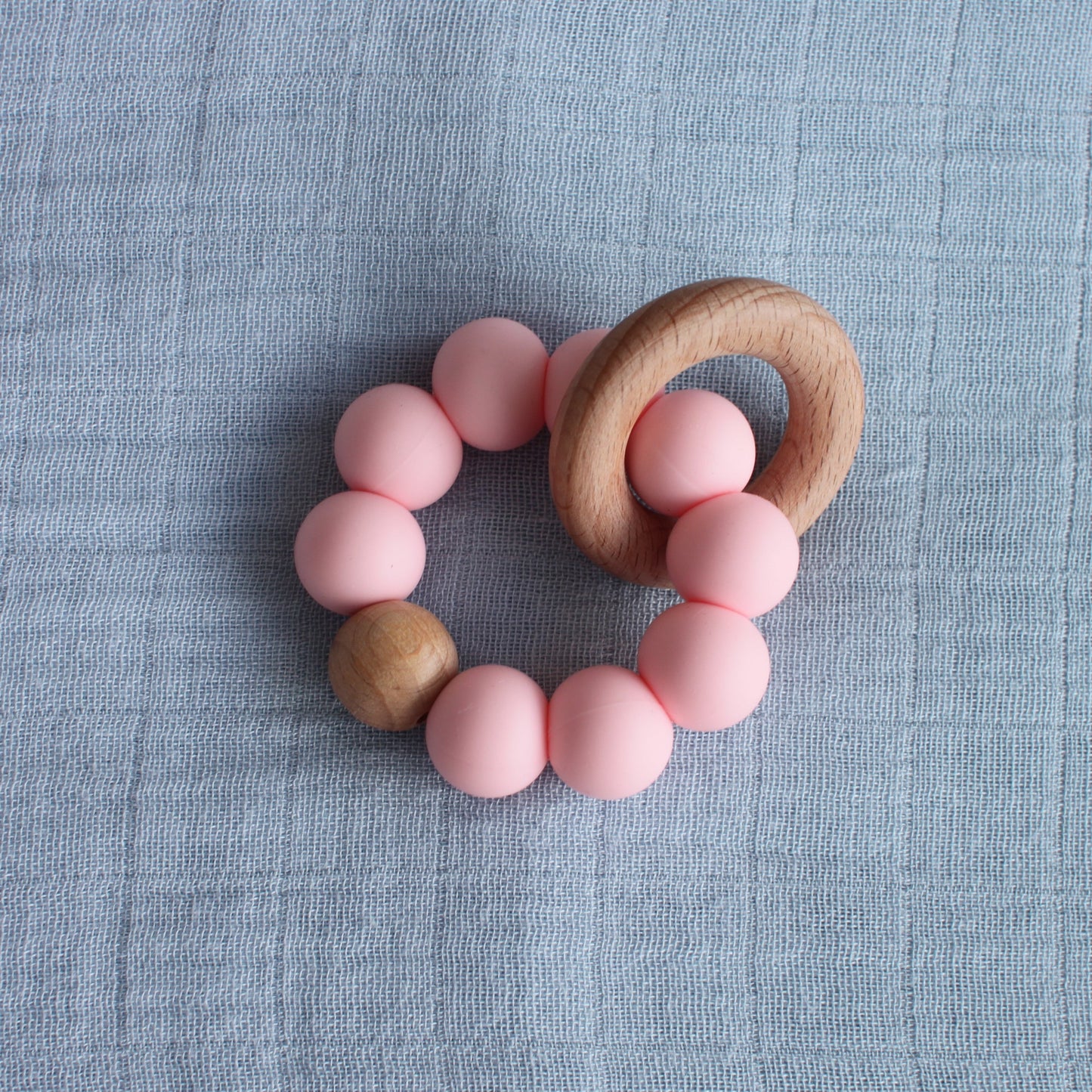 A silicone and beech wood teether. The silicone balls are pink. 