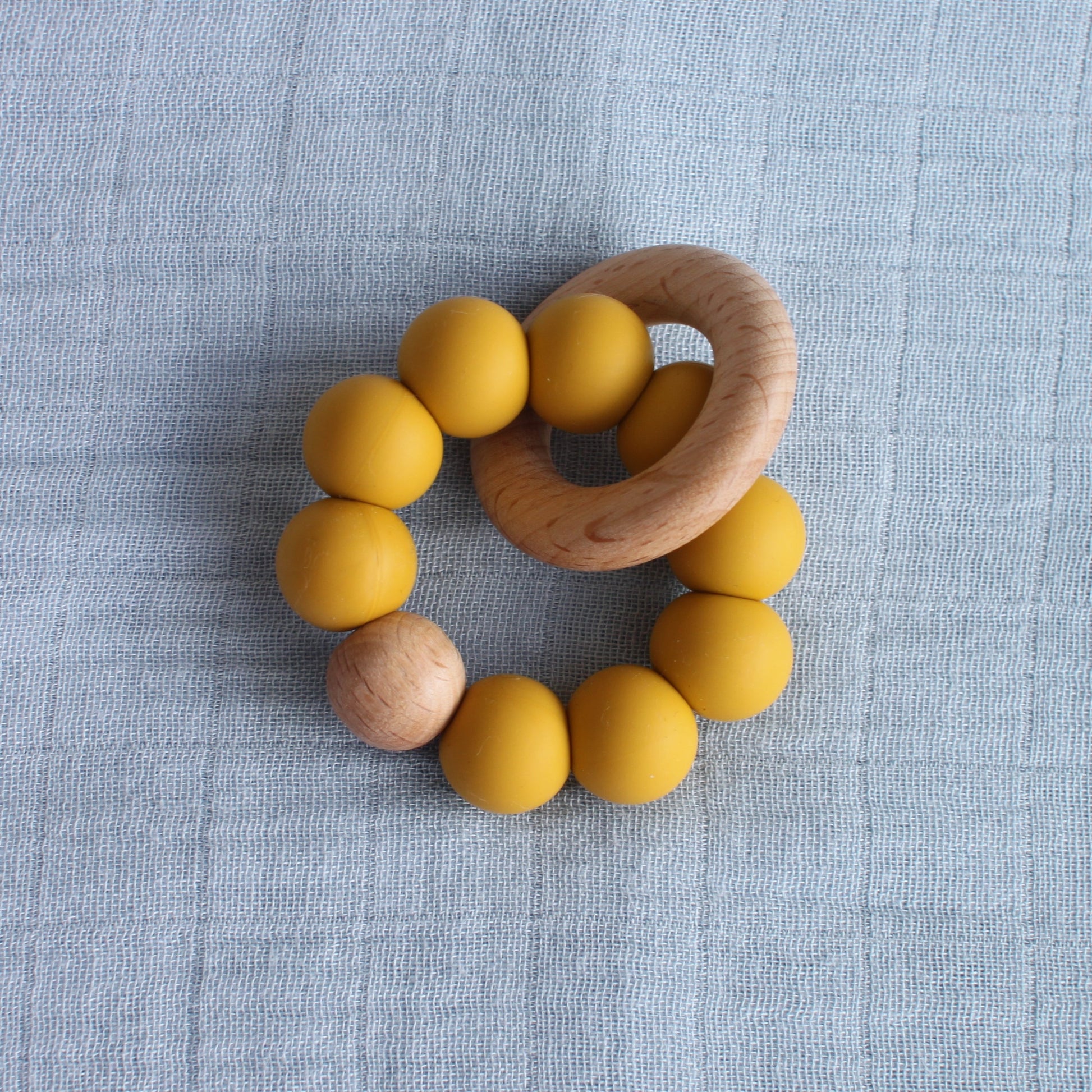 A silicone and beech wood teether. The silicone balls are yellow. 